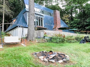 A house with a sloped roof, a chimney, and a backyard with a fire pit.