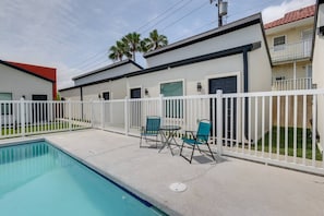 A swimming pool with a white fence, two chairs, and a table. - Modern South Padre Studio #4 - Blocks to Gulf/Pool - Apartment (South Padre Island)