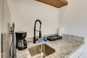 A kitchen with a stainless steel sink, a coffee maker, a kettle, and a stove. - Modern South Padre Studio #4 - Blocks to Gulf/Pool - Apartment (South Padre Island)