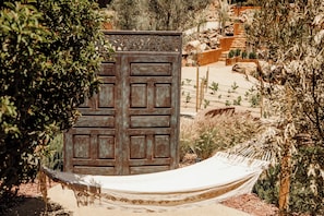 A hammock tied between two trees, a wooden gate, and a landscaped garden with various plants and rocks. - o2 Resort Valle de Guadalupe - King Cabana (B.C.)