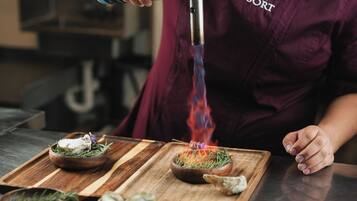 A person in a maroon shirt with a logo, pouring a liquid from a can into a device that emits blue flames.