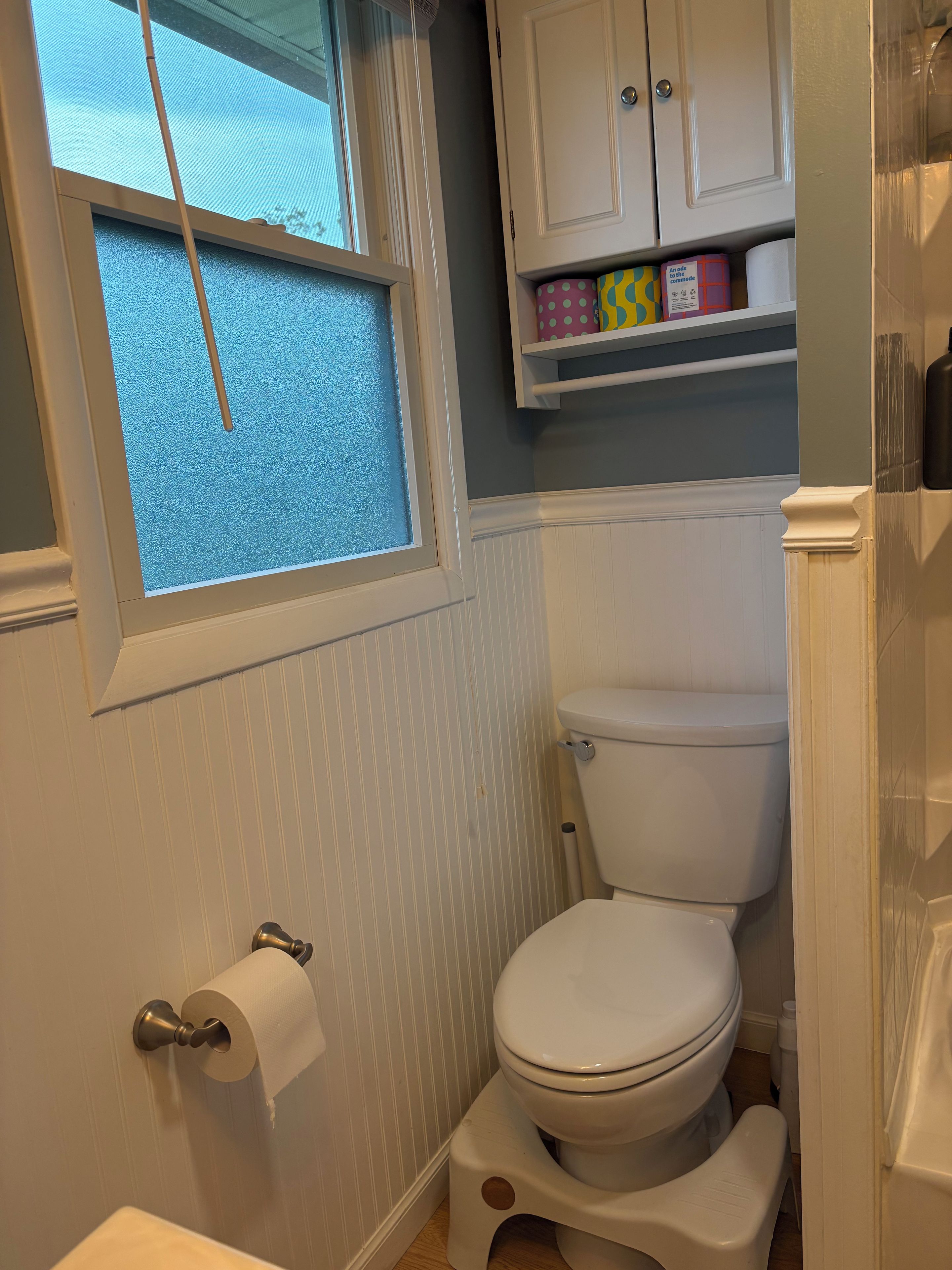 A bathroom with a toilet, a window, and a shelf with toiletries.