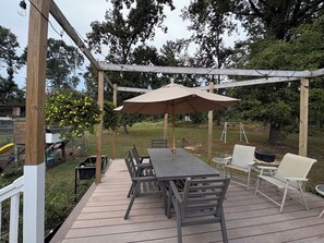 Eine Holzterrasse mit Tisch und Stühlen, umgeben von einer Pergola mit Lichterketten.