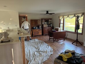Una habitación con un escritorio de madera, una estantería, una ventana con cortinas y un ventilador de techo.