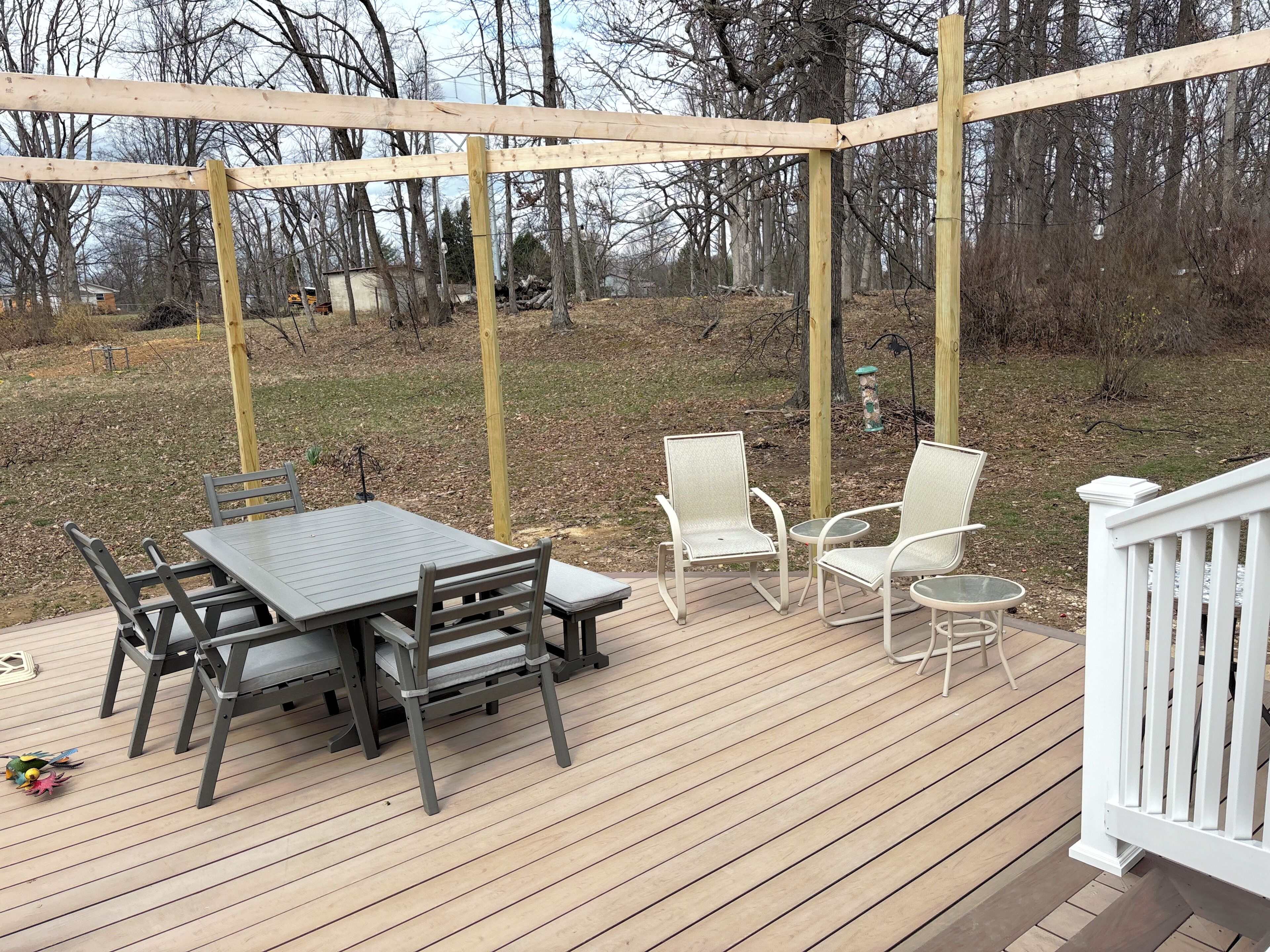 Une terrasse en bois avec une table et des chaises, entourée d’une balustrade blanche.