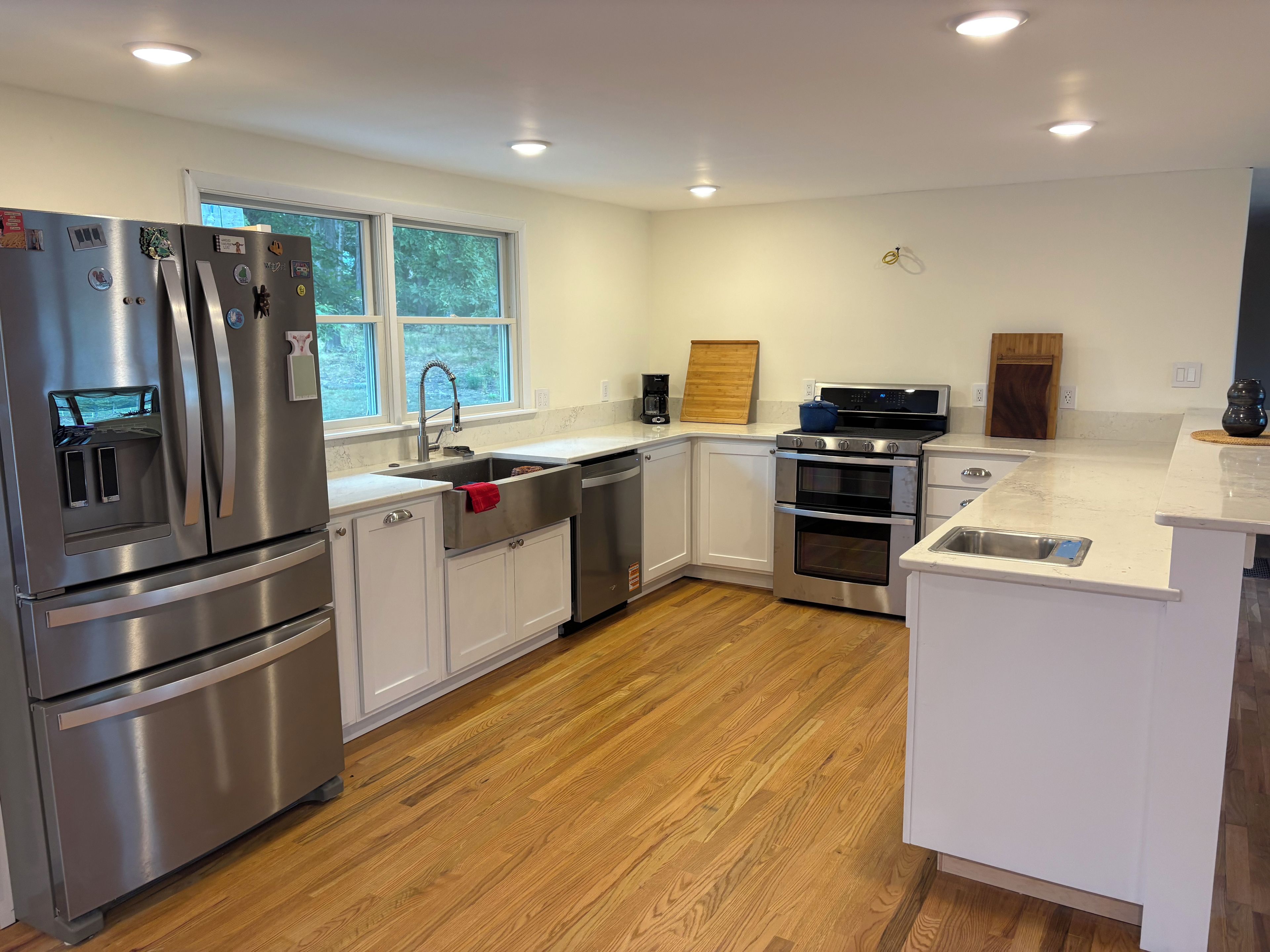 A modern kitchen with stainless steel appliances, a wooden floor, and a window providing natural light.