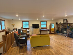 Un salon spacieux avec un plancher en bois, un canapé jaune, un téléviseur et une cheminée en pierre.