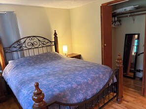 Ein Schlafzimmer mit einem Bett, einem Nachttisch, einer Lampe und einer Holztür, die in einen anderen Raum führt.