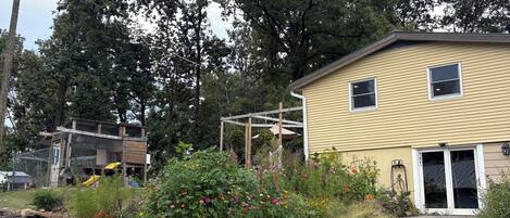 A residential area with a yellow house, a wooden structure, and a garden with various plants and flowers.
