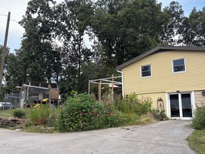 Ein Wohngebiet mit einem gelben Haus, einer Holzhütte und einem Garten mit verschiedenen Pflanzen und Blumen.