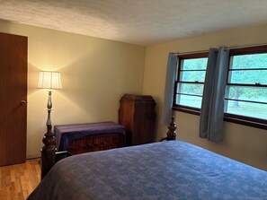 Un dormitorio con cama, mesita de noche, lámpara, armario y ventana con cortinas.