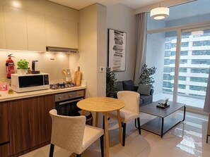 Eine moderne Küche mit Mikrowelle, Herd und Schränken. Ein Essbereich mit rundem Tisch und zwei Stühlen. Ein großes Fenster bietet Blick auf die Stadt.