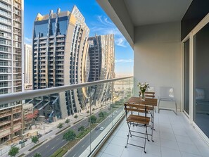 Ein Balkon mit Blick auf moderne Hochhäuser, einem Tisch mit Stühlen und einer Blumenvase.