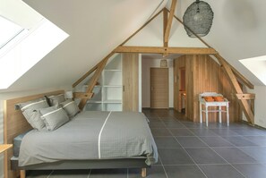 A bedroom with a sloped ceiling, a bed with patterned bedding, a wooden chair, and a hanging light fixture. - Charming cottage with sauna near Cambrai (Walincourt-Selvigny)