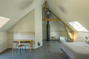 Ein Schlafzimmer im Loft-Stil mit schrägem Dach, einem Bett, einem Schreibtisch mit Stuhl, einem kleinen Tisch und einer Lampe.