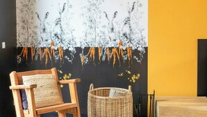 Quarto com um grande mural na parede, uma cadeira de madeira, um cesto de vime e um radiador preto.