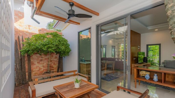 Eine Terrasse mit Holzmöbeln, einem Deckenventilator und einer Ziegelwand mit Pflanzen.