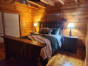 Ein Schlafzimmer einer Holzhütte mit einem Bett, zwei Nachttischen und einem Fenster mit Jalousien.