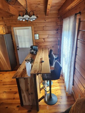 A wooden interior with a dining table, chairs, a refrigerator, and a window with curtains. - Stone & Legacy | Dollywood | Family Cabin (Sevierville)