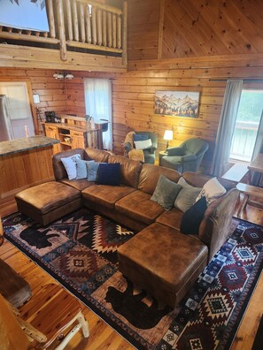 A cozy cabin interior with a wooden ceiling, a large sectional sofa, a dining area, and a painting on the wall. - Stone & Legacy | Dollywood | Family Cabin (Sevierville)