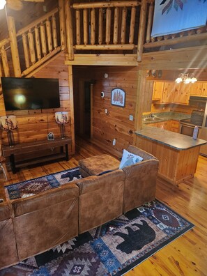 A cozy cabin interior with a wooden staircase, a living area with a sofa and rug, a kitchen with granite countertops, and a mounted flat-screen TV. - Stone & Legacy | Dollywood | Family Cabin (Sevierville)