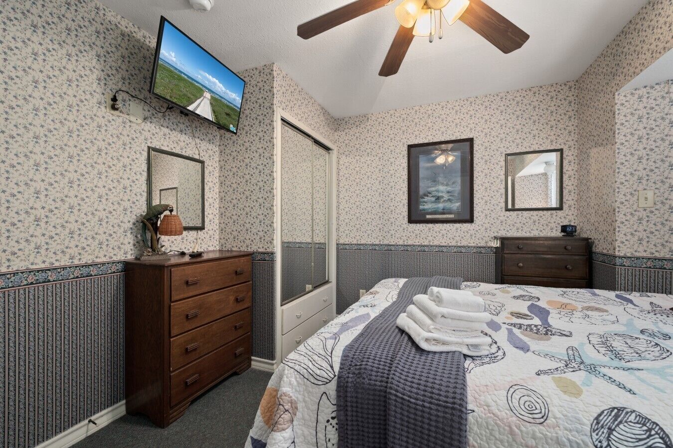 Une chambre à coucher avec un lit, une commode, un téléviseur et un ventilateur de plafond.