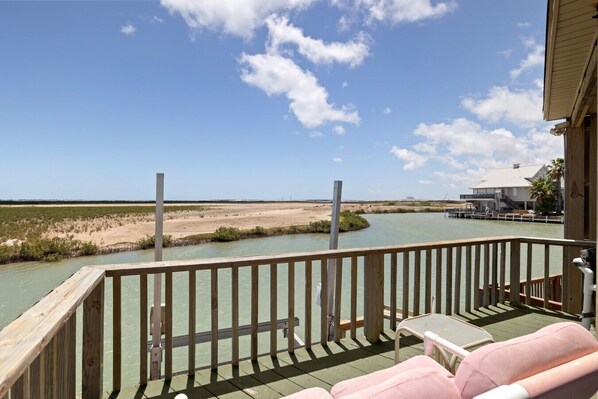 A wooden deck with a view of a water body and a distant building. - Oyster Cove in Long Island Village (Port Isabel)