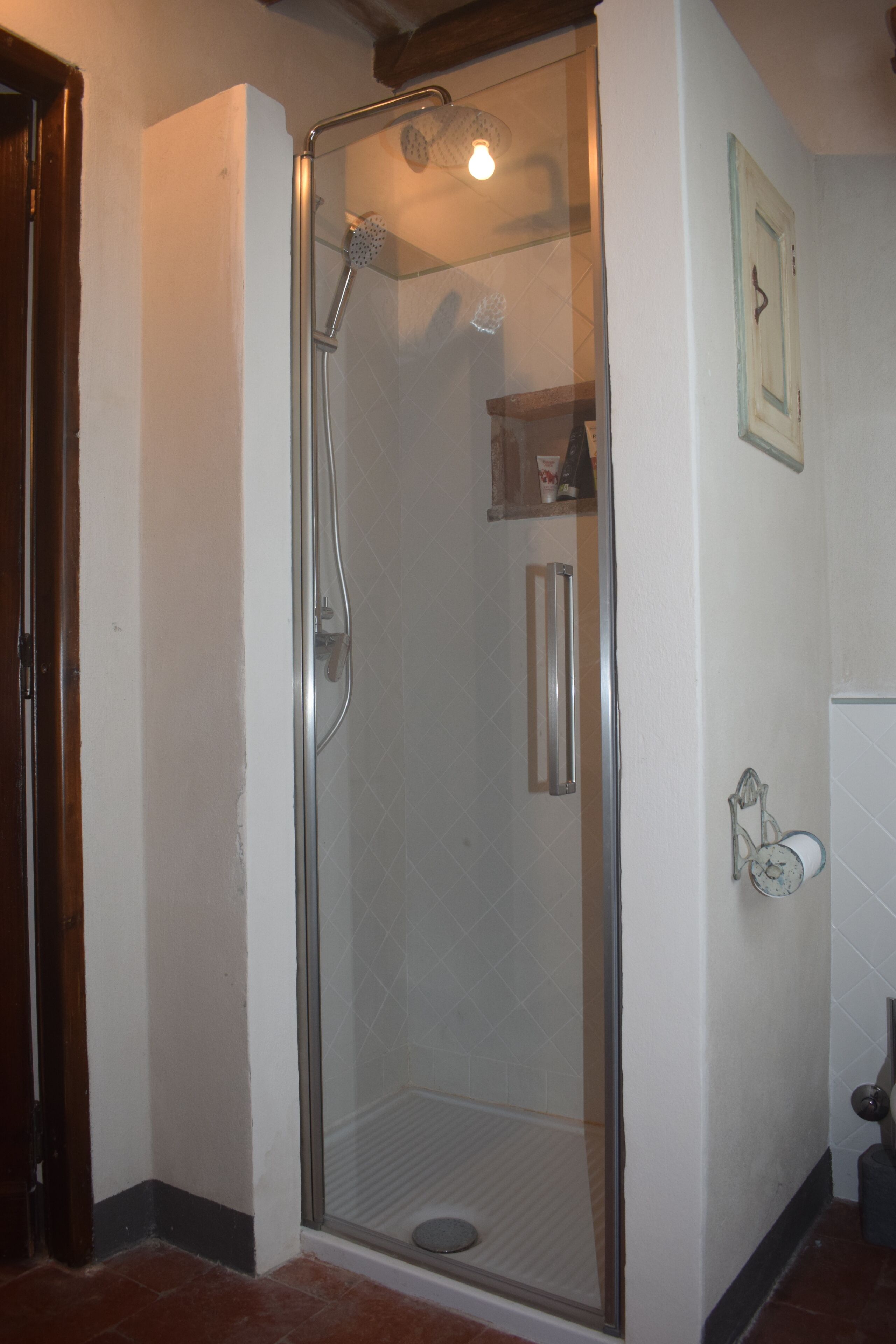 Eine Duschkabine mit Glaswänden, einer Handbrause und einem am Wand montierten Wasserhahn.