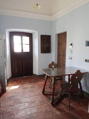 Una stanza con una porta in legno, un tavolo in vetro e una sedia. Sono presenti due interruttori a parete e una piccola mensola.