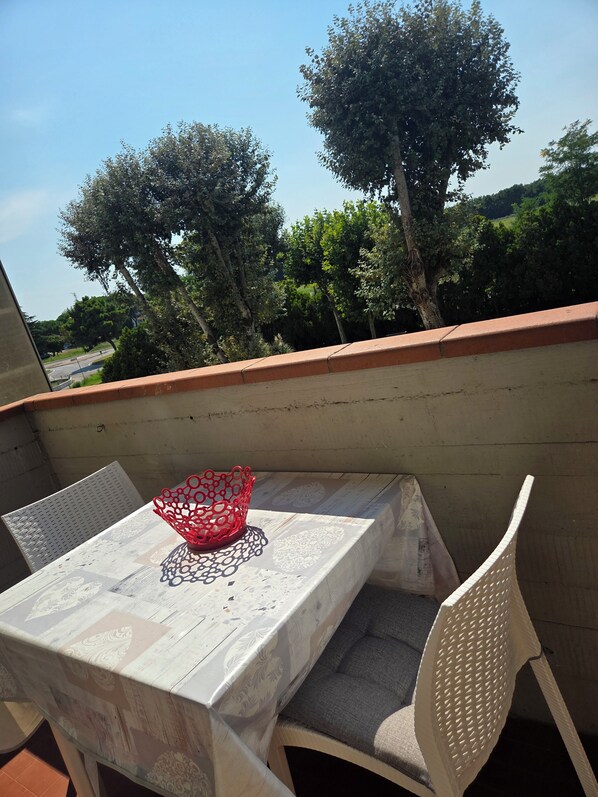 Un balcon avec une table et des chaises, un objet décoratif rouge, et une vue sur des arbres et une route.