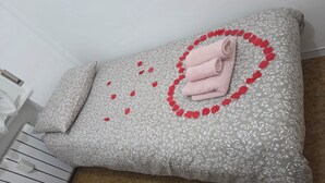A bed with a floral patterned bedspread, a rolled towel, and a decorative red heart design. - Apartment 300 meters from the beach, with air conditioning and a private parking space (Lido Adriano)