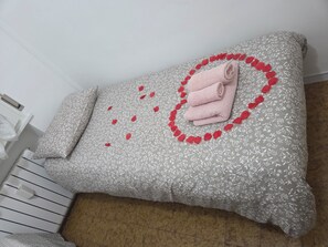 Ein Bett mit einem blumigen Bettbezug, ein gerolltes Handtuch und ein dekoratives rotes Herz.