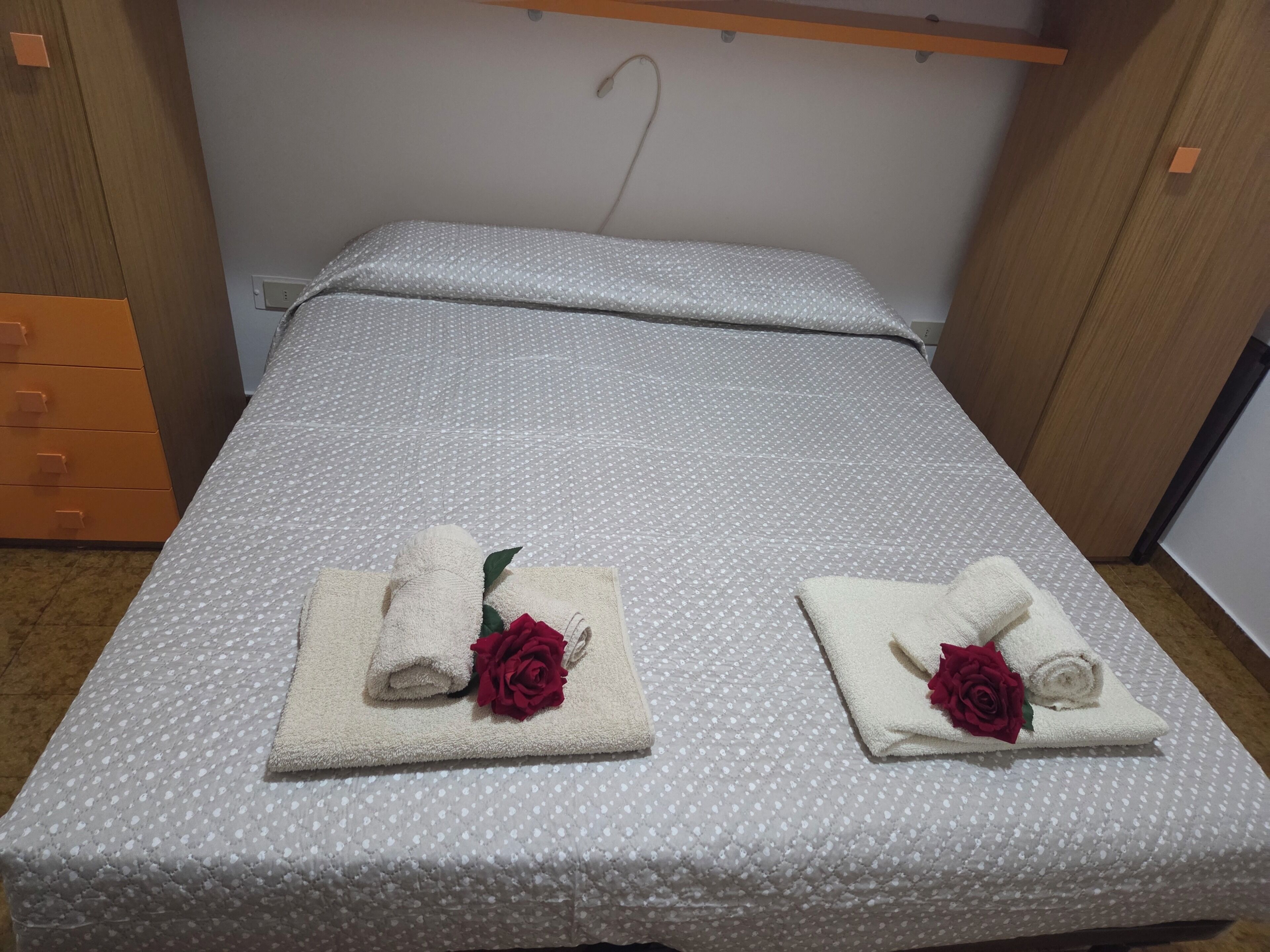 A single bed with a white quilt and two towels with red roses on each side.