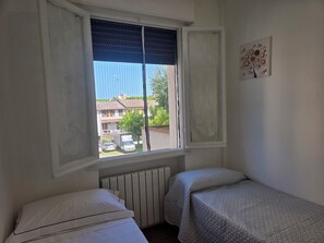 Ein Schlafzimmer mit Fenster, Heizkörper, Bett und einem an der Wand befestigten Kunstwerk.