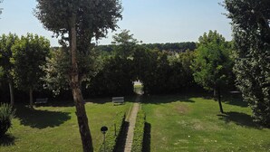 A courtyard with a paved path leading to a gate, surrounded by trees and parked cars. - Apartment 300 meters from the beach, with air conditioning and a private parking space (Lido Adriano)