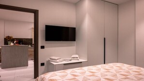 Ein modernes Schlafzimmer mit einem Bett, einem an der Wand montierten Flachbildfernseher, einem Nachttisch mit Handtuch und einem Kleiderschrank.