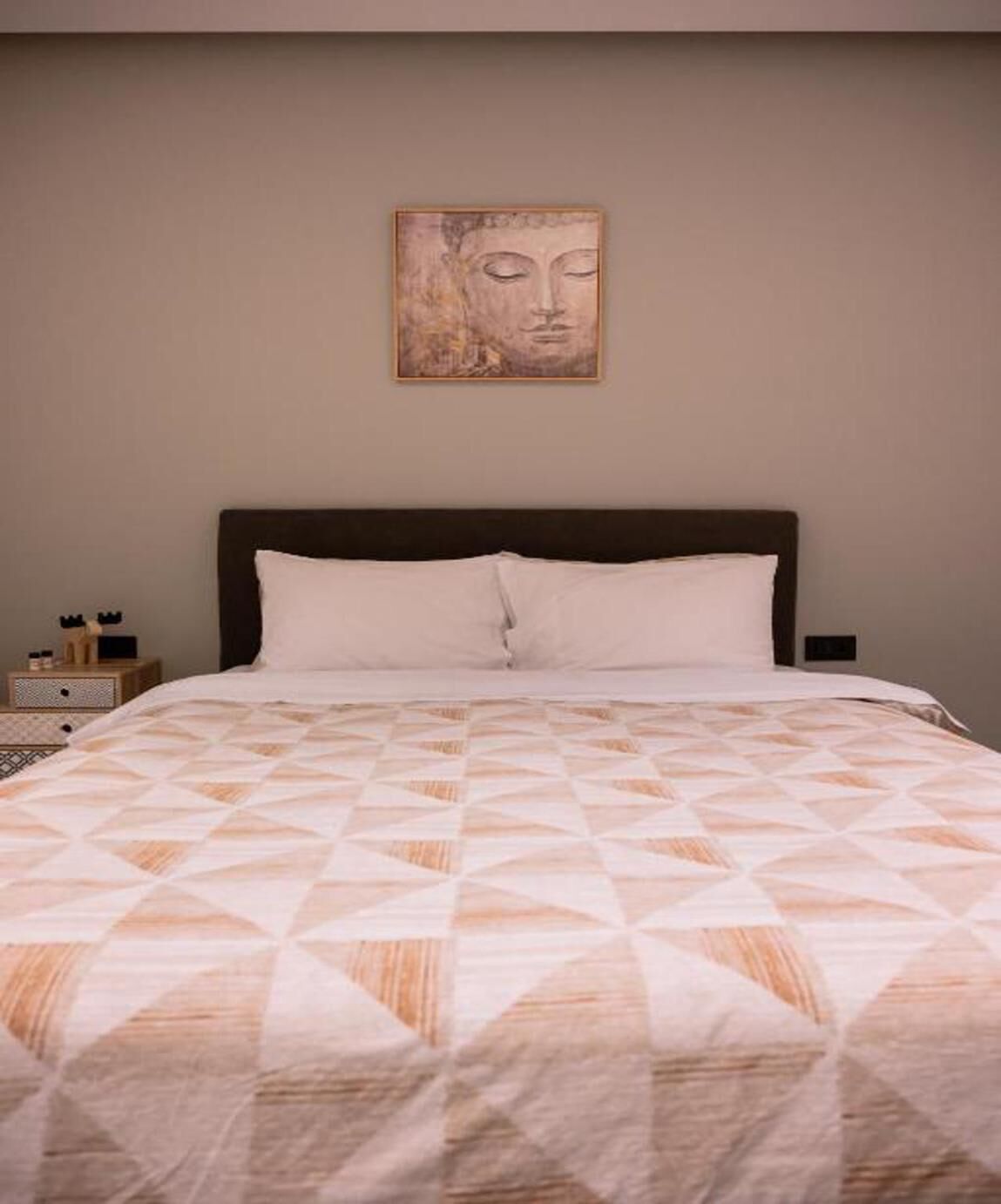 A bed with a geometric patterned bedspread, a dark headboard, and a wall-mounted artwork above it.