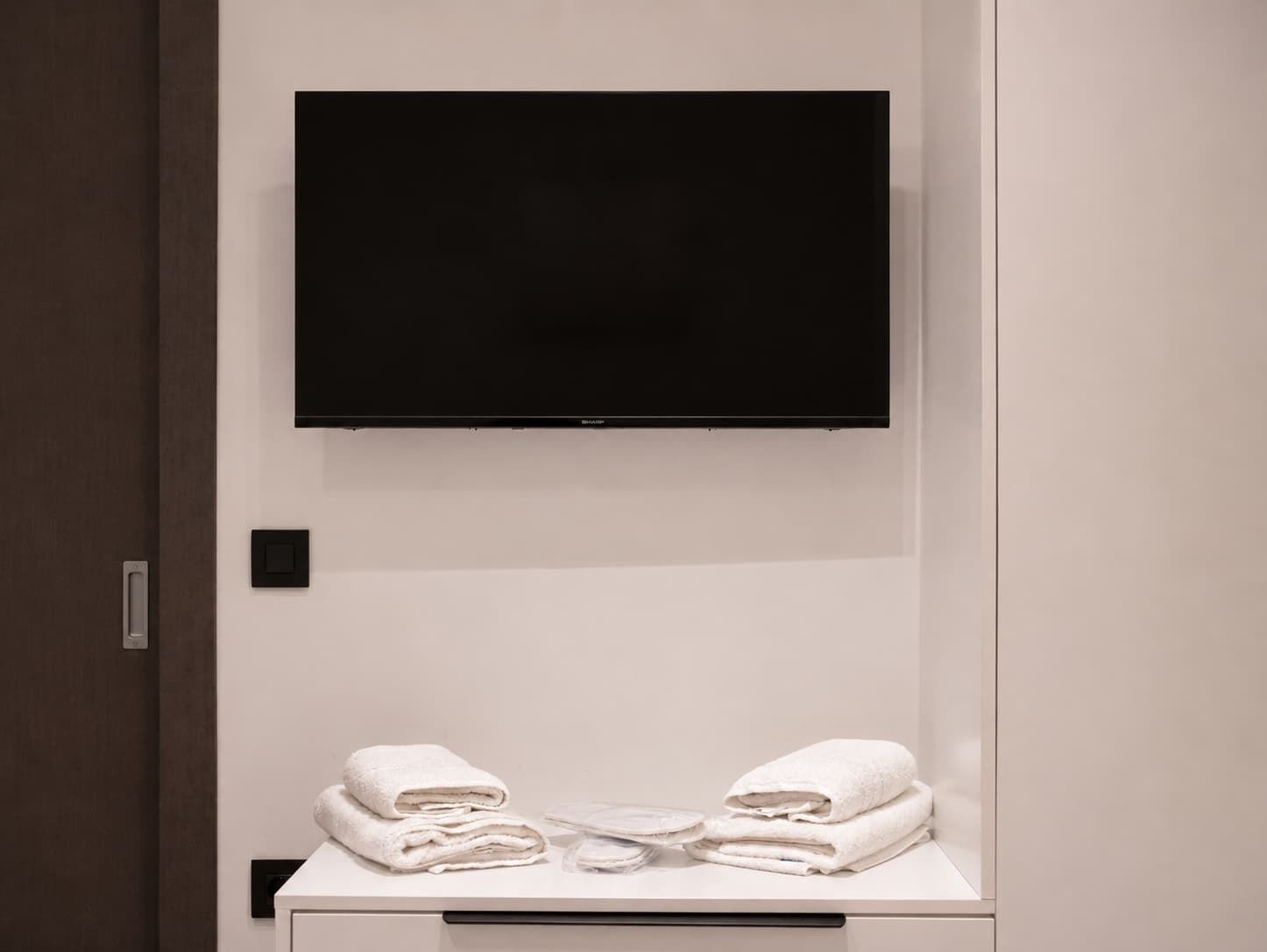 Ein modernes Badezimmer mit einem an der Wand montierten Flachbildfernseher, einem Handtuchhalter mit gefalteten Handtüchern und einer Bedienkonsole an der Wand.