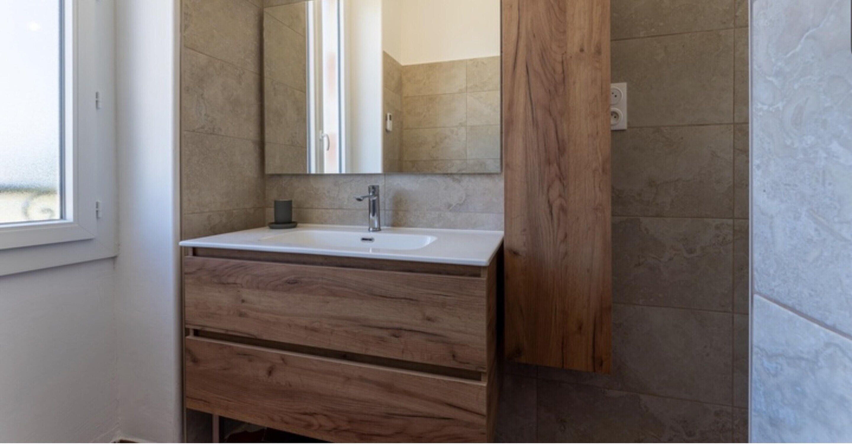 A bathroom with a white sink, wooden vanity, and a mirror.
