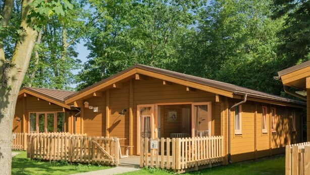 Een houten hut met een veranda, een omheinde tuin en een heldere lucht.