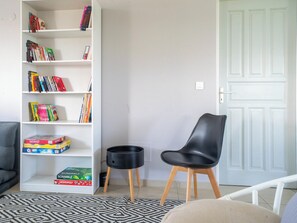 Een woonkamer met een witte boekenkast vol boeken en spellen, een zwarte stoel, een kamerkleed met patroon en een witte deur.