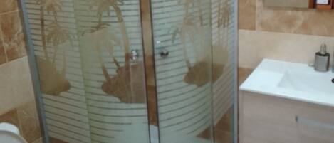 A bathroom with a glass-enclosed shower, a toilet, and a sink with a mirror.