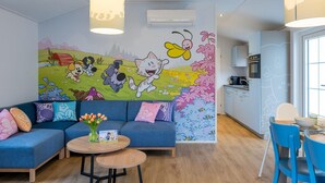 A modern living room with a blue sofa, a round wooden table, and a colorful mural on the wall. - Family Holiday Home in Resort in Hoogerheide (Hoogerheide)