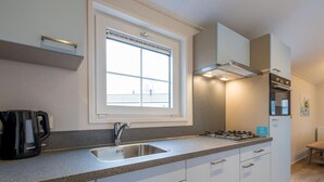 A modern kitchen with a window, stainless steel sink, gas stove, and white cabinetry. - Family Holiday Home in Resort in Hoogerheide (Hoogerheide)