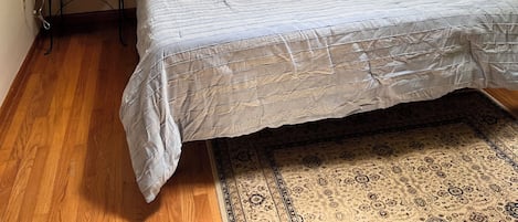 A bedroom with a bed, two bedside tables, a lamp, a ceiling light, and a patterned rug.