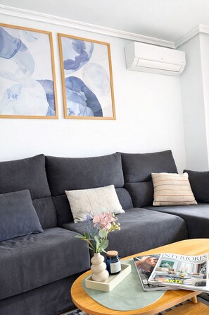 Un salon moderne avec un canapé gris, deux tableaux abstraits encadrés, une petite table avec un magazine et un vase décoratif rempli de fleurs.