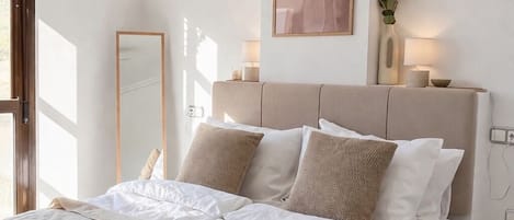 Un dormitorio con cama, mesitas de noche, ventilador de techo, aire acondicionado instalado en la pared, una obra de arte enmarco y una planta en maceta.