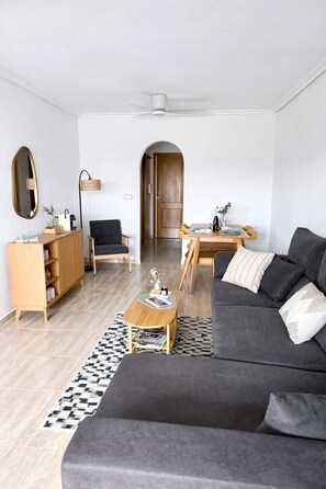 Ein modernes Wohnzimmer mit grauem Sofa, einem Holztisch und einem Essbereich mit Holztisch und Stühlen.