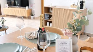 A dining table set with plates, glasses, a bottle of champagne, a candle, and a menu card in a modern, well-lit room with a television and a mirror on the wall. - Peaceful 2-Bedroom Apartment, Shared Pool, Balcony, Torrevieja, Alicante (Torrevieja)