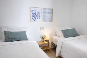 Ein Hotelzimmer mit zwei Betten, weißer Bettwäsche, einem Nachttisch mit Lampe und zwei gerahmten Bildern an der Wand.